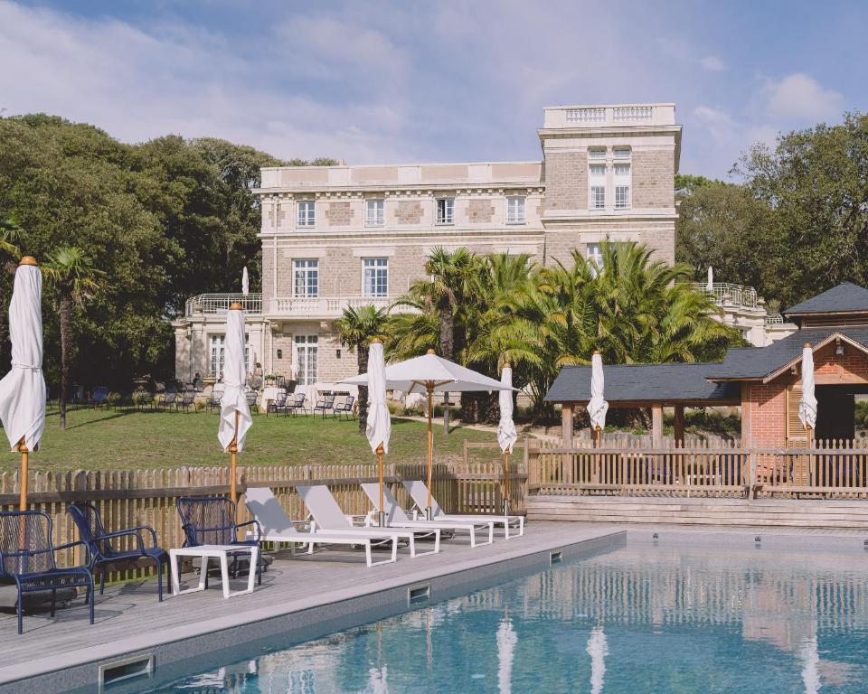 - une piscine avec des chaises et des parasols en face d'un bâtiment dans l'établissement Villa Arthus-Bertrand, à Noirmoutier-en-l'lle