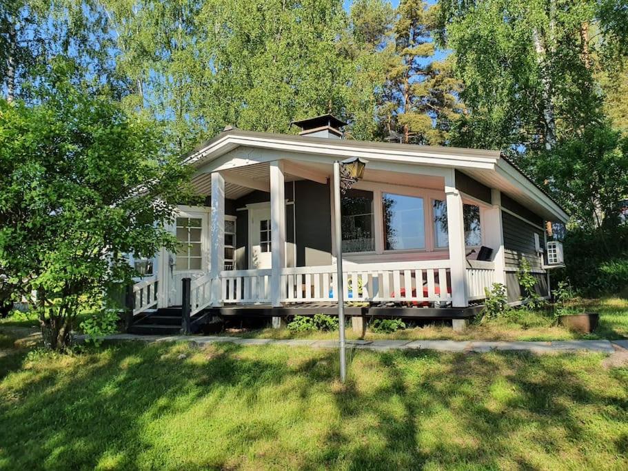 een klein huis met een witte veranda en een tuin bij Mökki ja rantasauna Saimaan rannalla in Taipalsaari