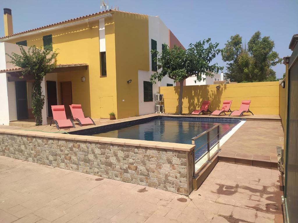 a swimming pool with chairs and a house at Casa familiar con piscina, cerca de la playa in Ciutadella