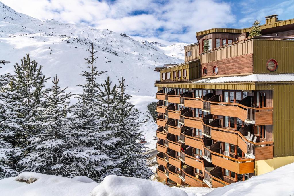 a building in the snow with a mountain in the background at Hôtel Les Menuires Les Bruyères in Les Menuires