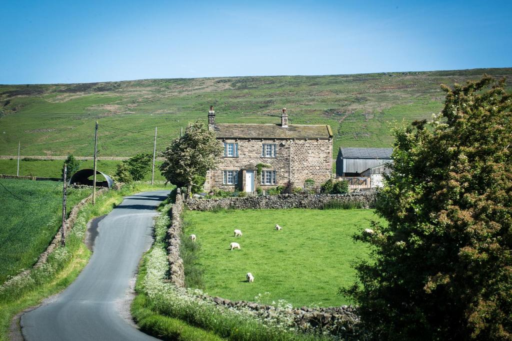 a stone house with sheep in the grass next to a road at Crown Cottage Farm in Skipton