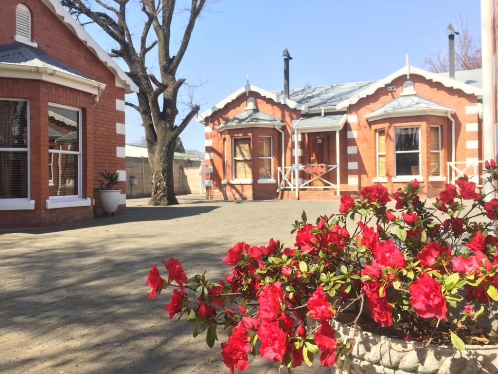 una casa de ladrillo con flores rojas delante de ella en Tom's Place Guest House, en Harrismith