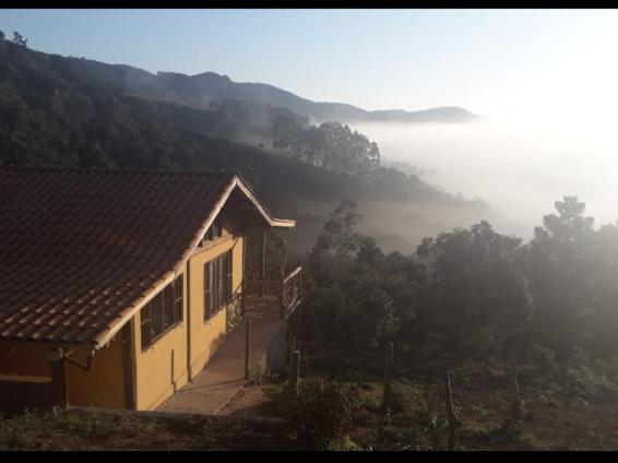 ein Haus auf einem Hügel mit Blick auf ein nebliges Tal in der Unterkunft Chalé Sabiá in Aiuruoca