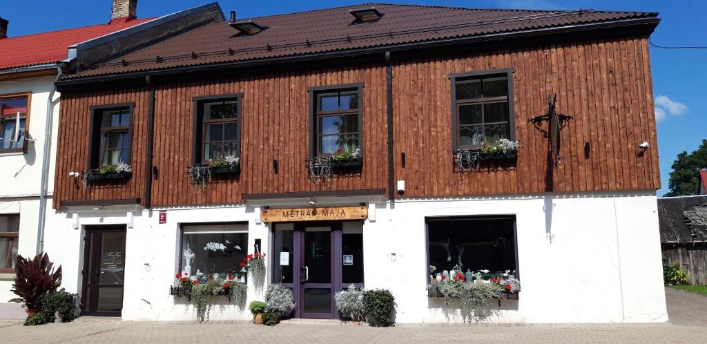 a wooden building with flowers in the windows at Mētras Māja in Aizpute