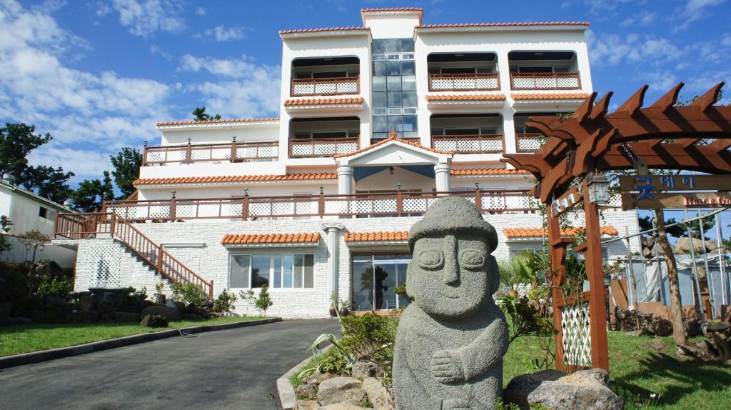 - un grand bâtiment blanc avec une statue devant dans l'établissement Good Day Pension, à Seogwipo