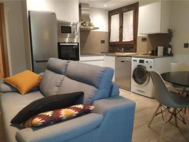uma sala de estar com um sofá azul e uma cozinha em CHECK-IN CASAS La Tuca em Benasque