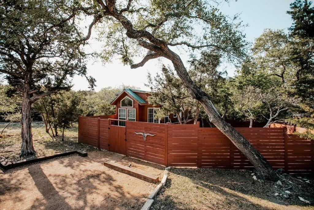 uma árvore inclinada sobre uma cerca com uma casa em The Longhorn Cabin - Cabins at Rim Rock em Austin