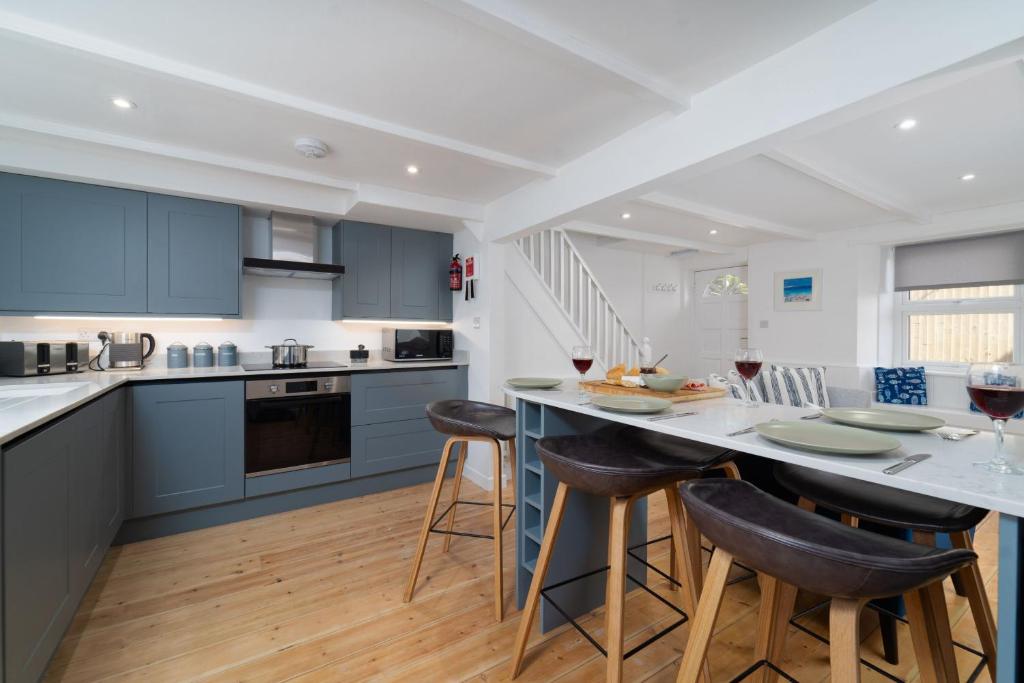 a kitchen with blue cabinets and a table with bar stools at Karibu - Boutique Cottage with Parking - Short walk to Beach in St Ives