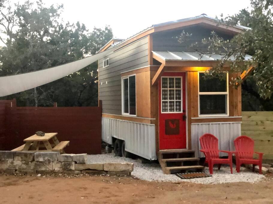 a tiny house with a red door and two red chairs at Fox Tiny Home - The Cabins at Rim Rock in Austin