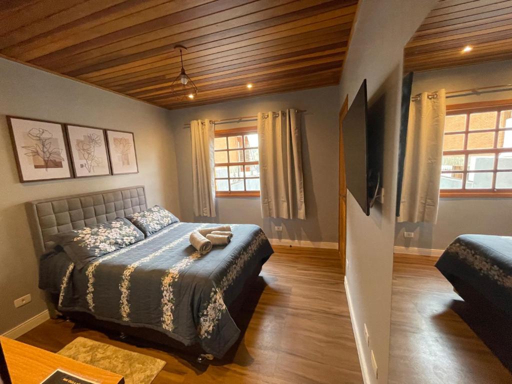 Schlafzimmer mit einem Bett, einem Tisch und Fenstern in der Unterkunft Suítes Paz na Montanha - Tesouro Escondido in Campos do Jordão