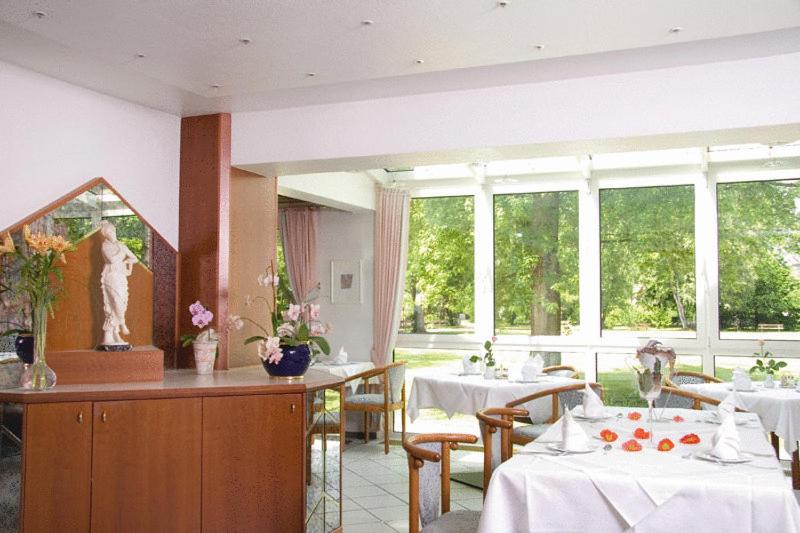un restaurante con mesas y sillas blancas y ventanas en Kurhotel Kaiser, en Bad Wörishofen