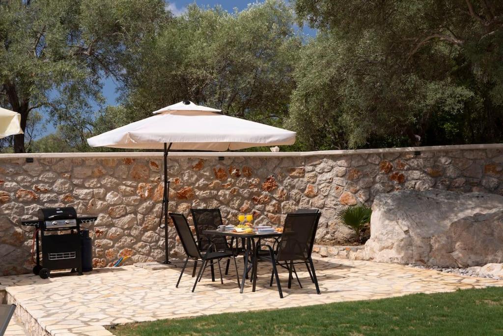 a table and chairs with an umbrella next to a stone wall at Lefkolia Retreat in Sivota