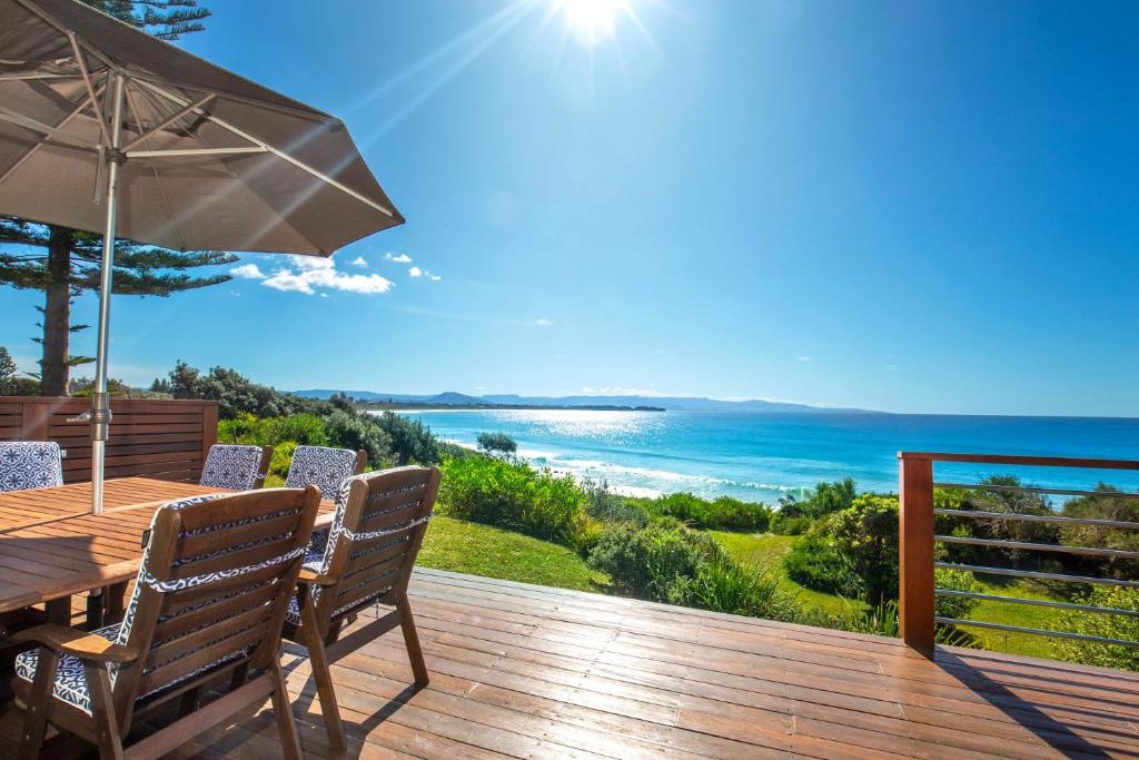 a wooden deck with a table and an umbrella at Eclipse Absolute Beachfront with Stunning Views in Culburra Beach