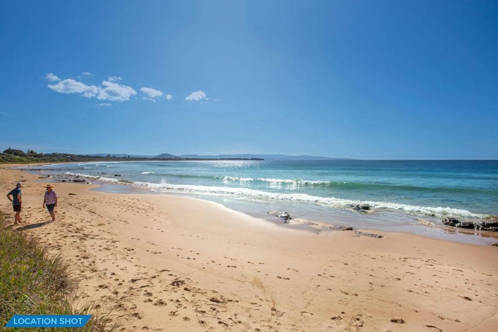 two people walking on a sandy beach near the ocean at Eclipse Absolute Beachfront with Stunning Views in Culburra Beach