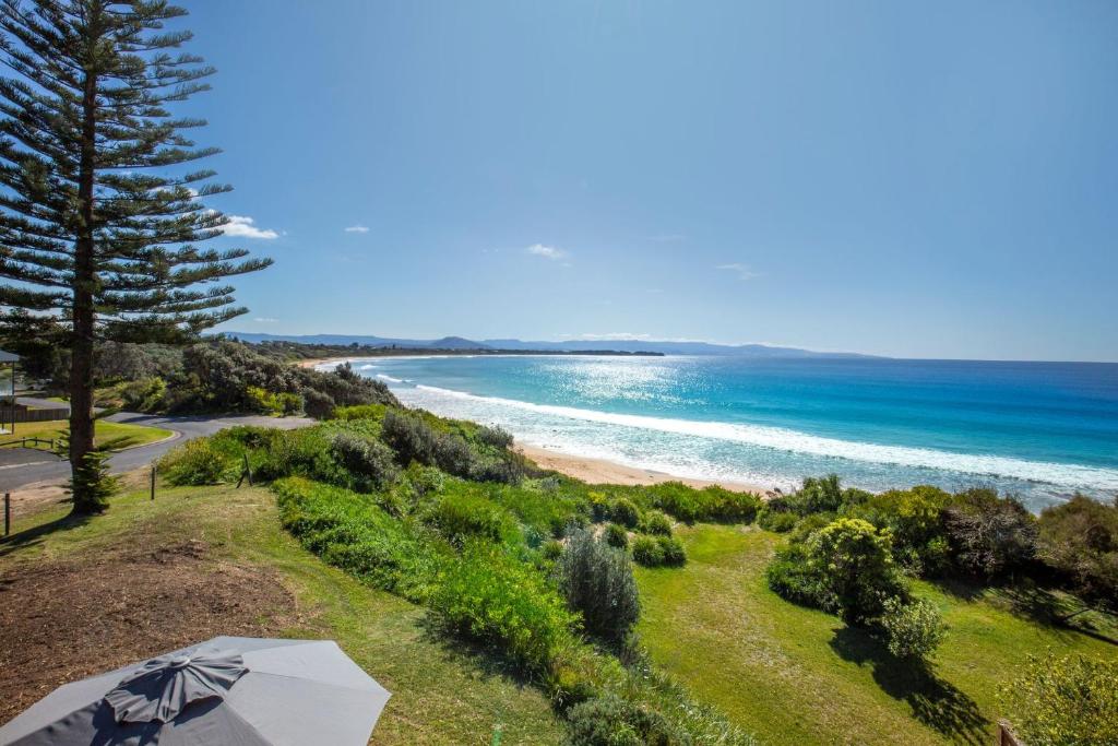 a beach with an umbrella and the ocean at Eclipse Absolute Beachfront with Stunning Views in Culburra Beach