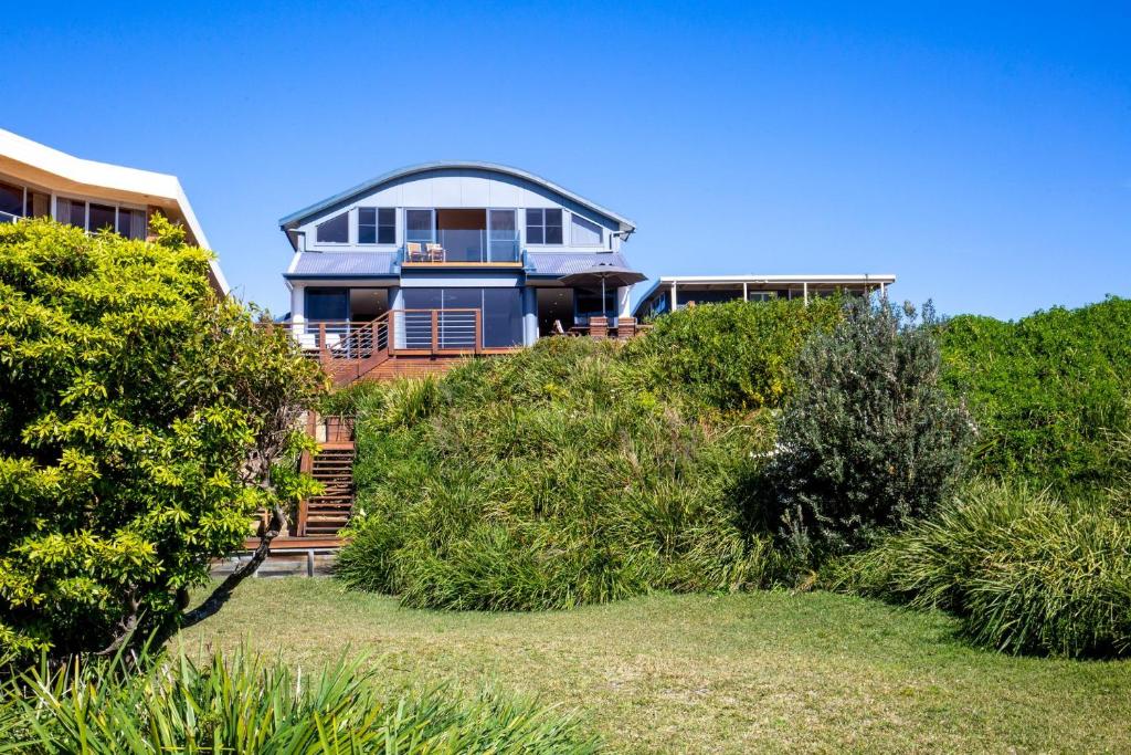 a large house on top of a hill with bushes at Eclipse Absolute Beachfront with Stunning Views in Culburra Beach