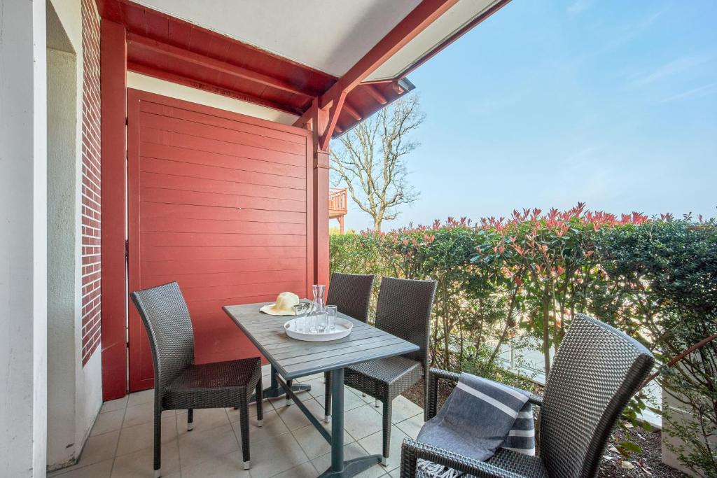 a table and chairs on a patio with a red wall at Pierre & Vacances Premium Residence & Spa Houlgate in Houlgate