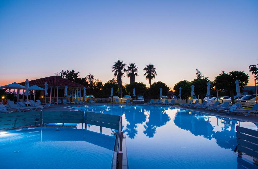 a large swimming pool with chairs and palm trees at Acrotel Lily Ann Village in Nikiti