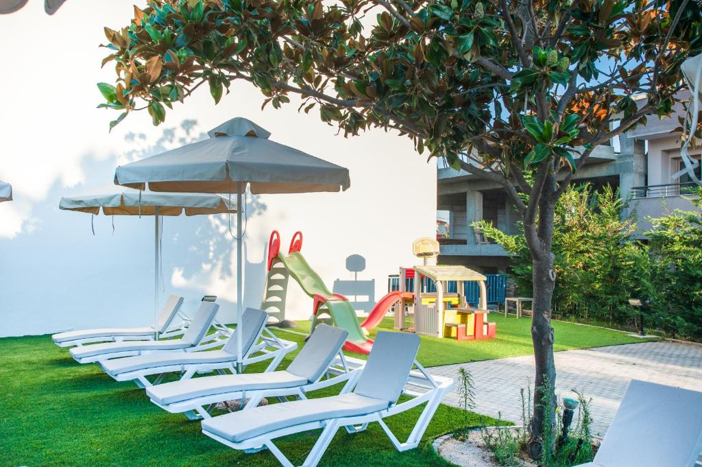 a row of lounge chairs with an umbrella and a playground at Acrotel Lily Ann Village in Nikiti