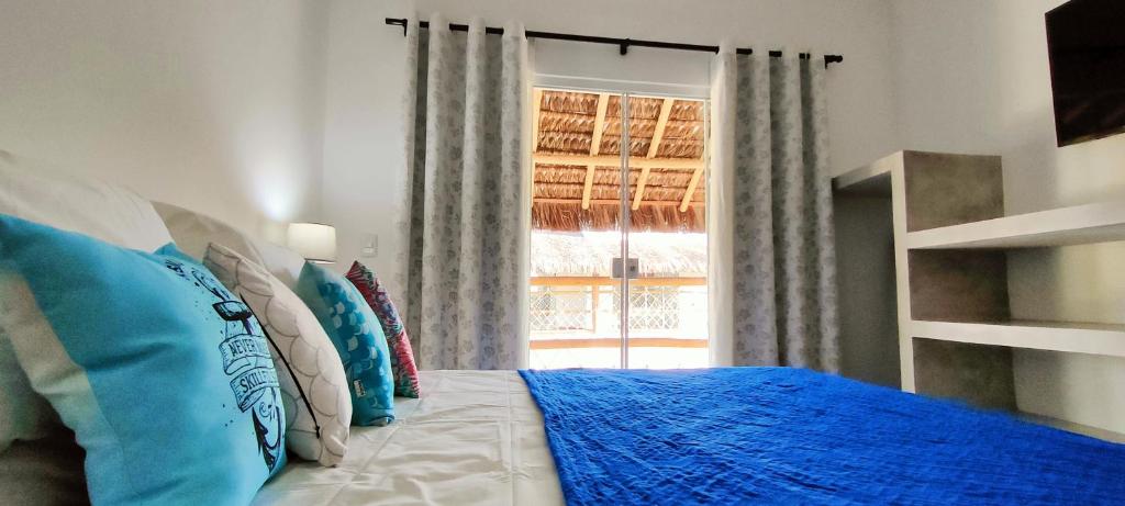 a bedroom with a bed with blue pillows and a window at Sirena Village in São Miguel do Gostoso