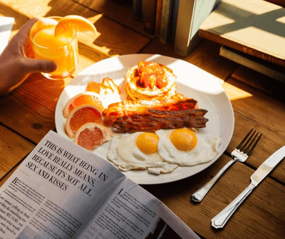 a plate of breakfast food on a table with a book at Sphinx Apartment in Visoko