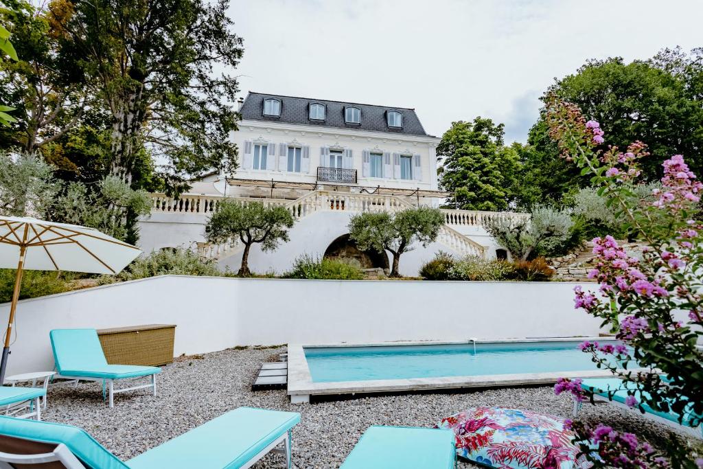 a pool in front of a white wall with chairs and a house at Manoir d&#39;Amaury - Chambres d&#39;hôtes in Gréoux-les-Bains
