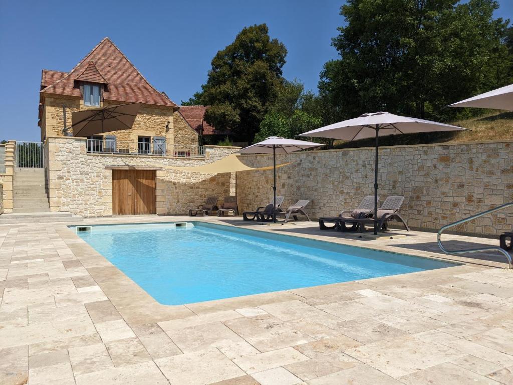 une piscine avec deux parasols et un bâtiment dans l'établissement Domaine de Fleurie, à Tursac