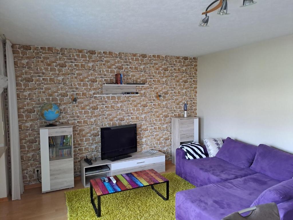 ein Wohnzimmer mit einem lila Sofa und einer Ziegelwand in der Unterkunft Ferienwohnung Schleiten in Püttlingen