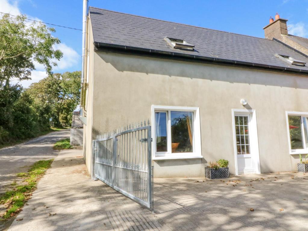 a white house with a fence next to a street at Beehive Cottage in Kilbrittain