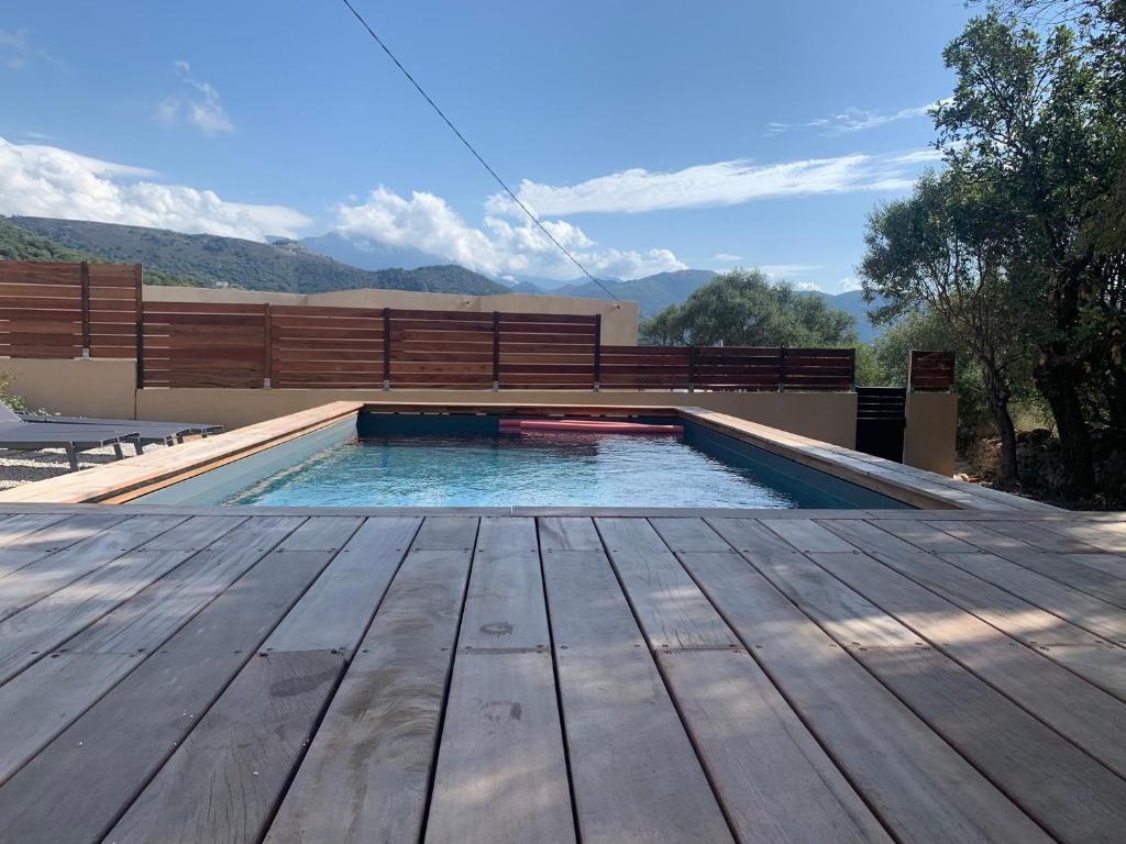 a swimming pool with a wooden deck and a bench at Maison neuve avec piscine in Corbara