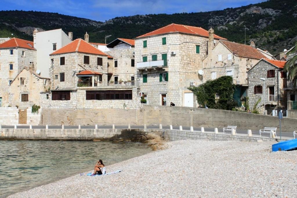 a woman sitting on a beach next to the water at Apartments and rooms by the sea Komiza, Vis - 8910 in Komiža