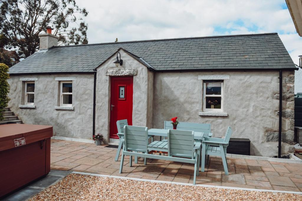 una casa con mesa, sillas y puerta roja en Lizzie's Cottage, en Drumaroad