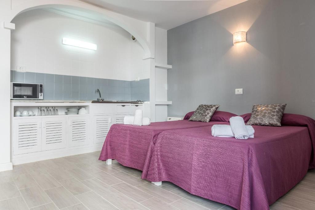 a bedroom with two beds with purple sheets and a kitchen at Apartamentos Orosol 2 in San Antonio