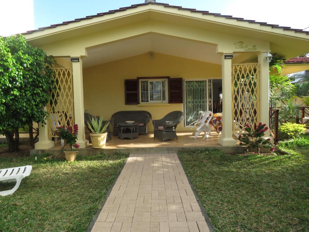 una pequeña casa amarilla con porche y sillas en VILLA CANELLE, en Trou aux Biches