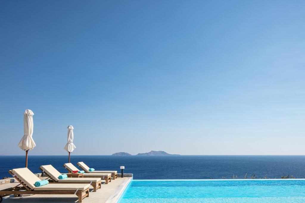 Seafront elegant villa, with infinity pool & devine views! في أجيوس بافلوز: صف كراسي الجلوس بجانب المسبح