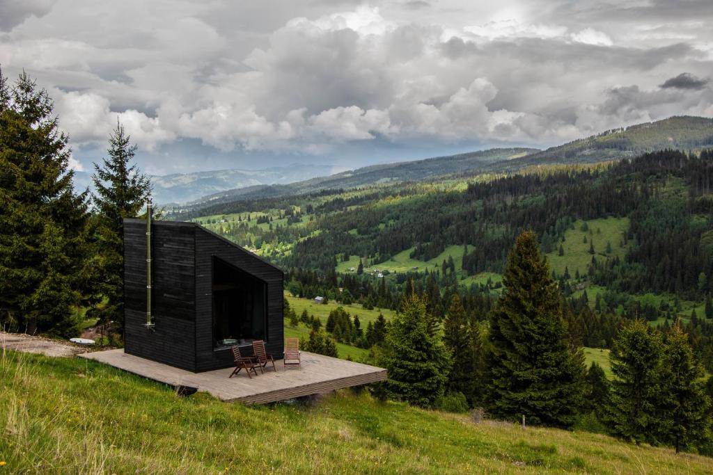 a small black cabin on a hill with trees at Haita Land in Vatra Dornei
