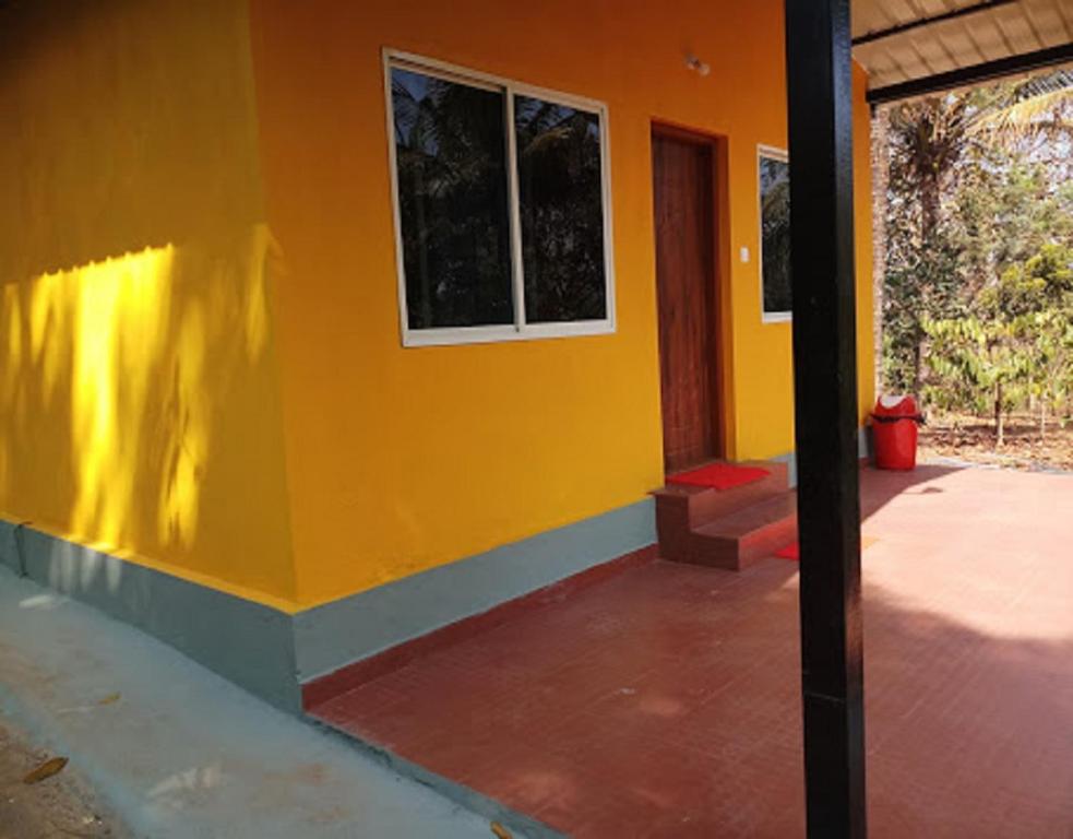 a house with a yellow wall and a porch at Hasiru Farms Homestay by StayApart in Mudigere