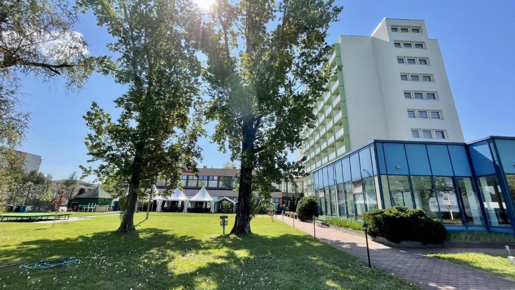um edifício com árvores em frente a um edifício em Hotel Magistern Konferencia és WellnessHotel em Siófok