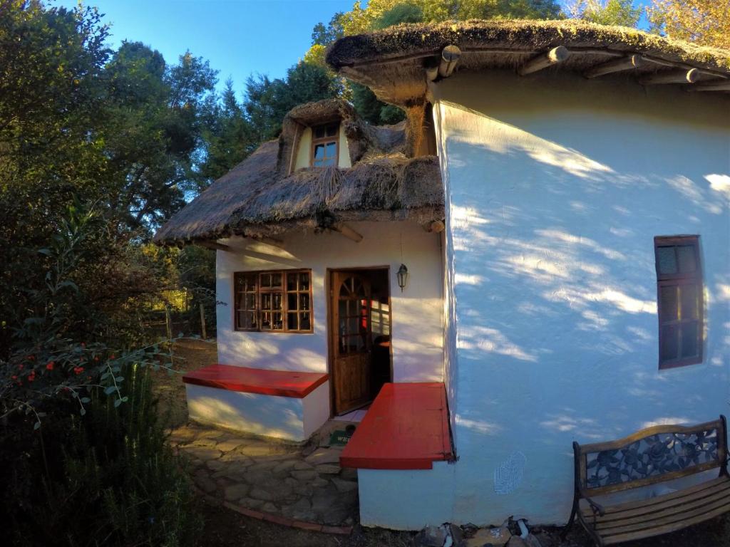 een klein huis met een rieten dak en een rode veranda bij Gryffin Cottage at Hogwarts Forest in Hogsback