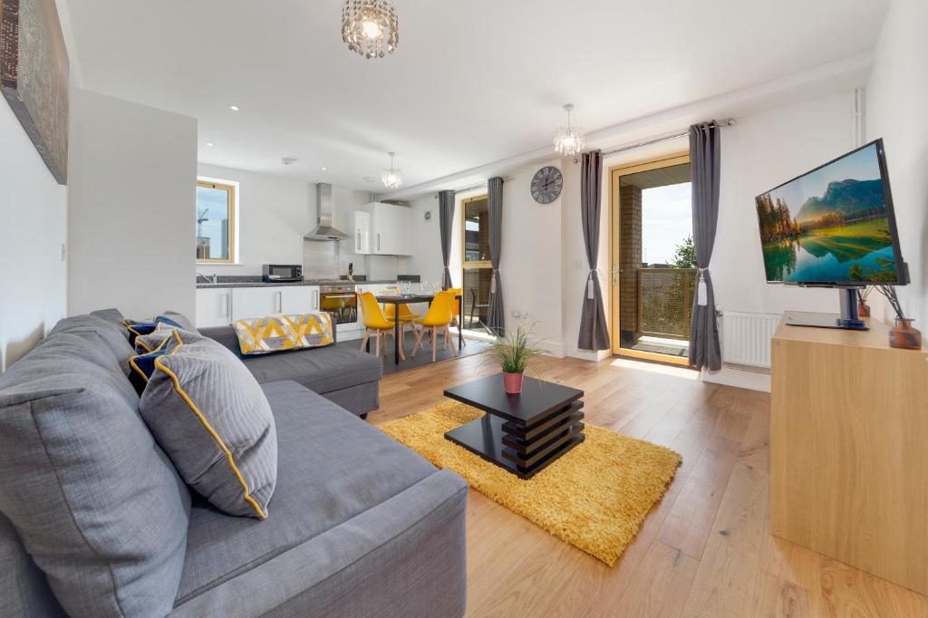 a living room with a gray couch and a tv at Flourish Apartments - Mulberry House - Tottenham in London