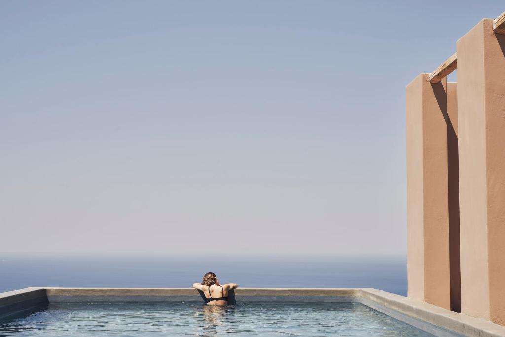 a woman is standing in a swimming pool at Under the Sun Cycladic Village in Tinos