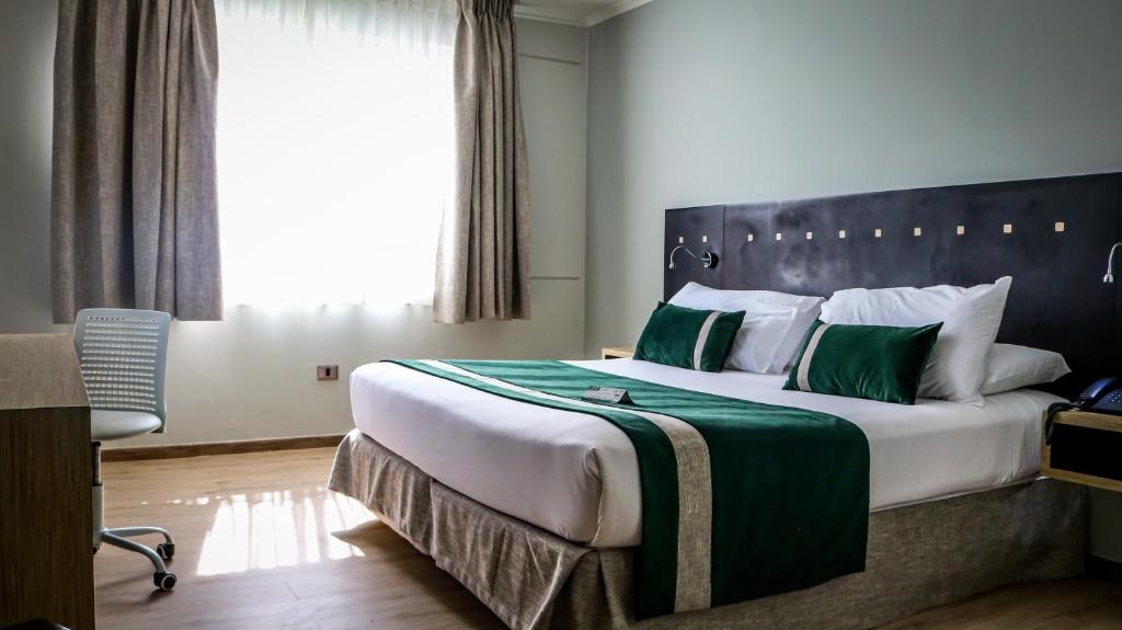 a bedroom with a large bed with green and white pillows at Ecohotel Talca in Talca