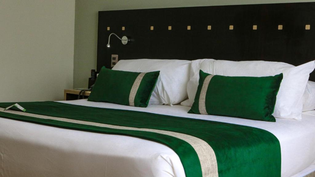 a large bed with green and white sheets and pillows at Ecohotel Talca in Talca