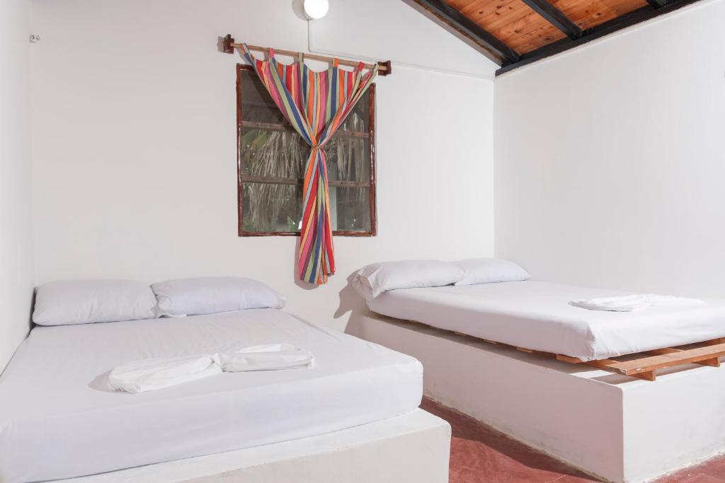 two beds in a white room with a window at Casa Grande Surf in Guachaca