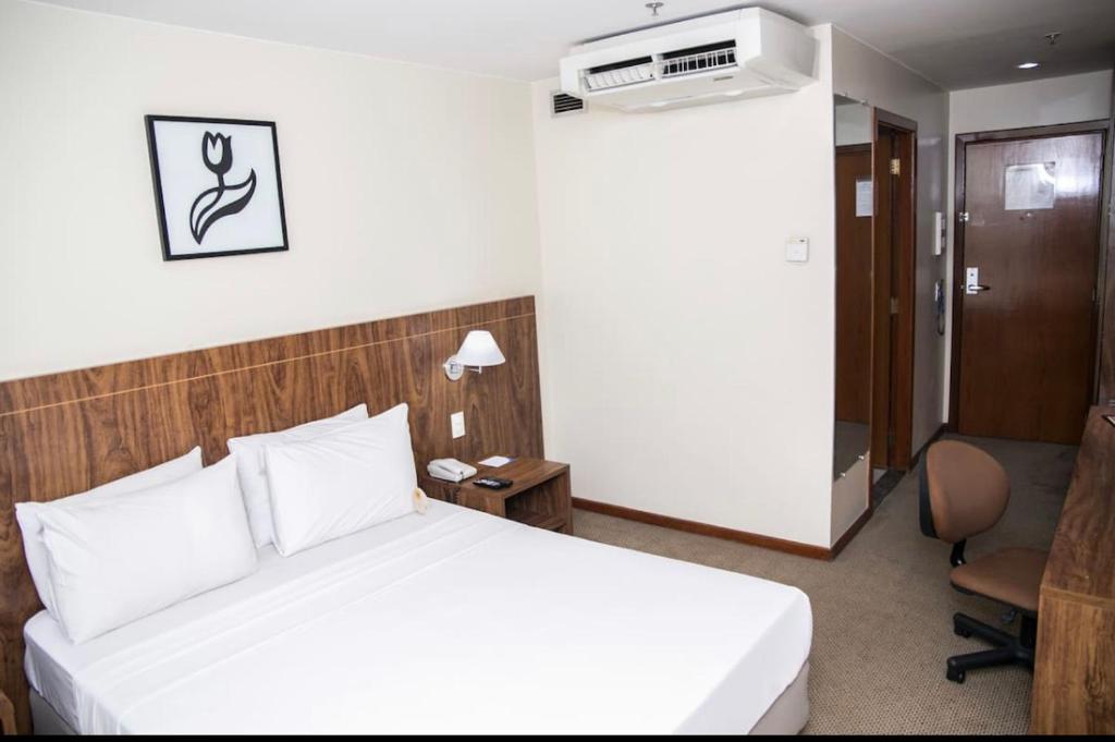 a hotel room with a white bed and a desk at PROMOÇÃO EXECUTIVA COM BANHEIRA E FLATS SEM BANHEIRA- Melhor Hotel De Taguatinga in Taguatinga