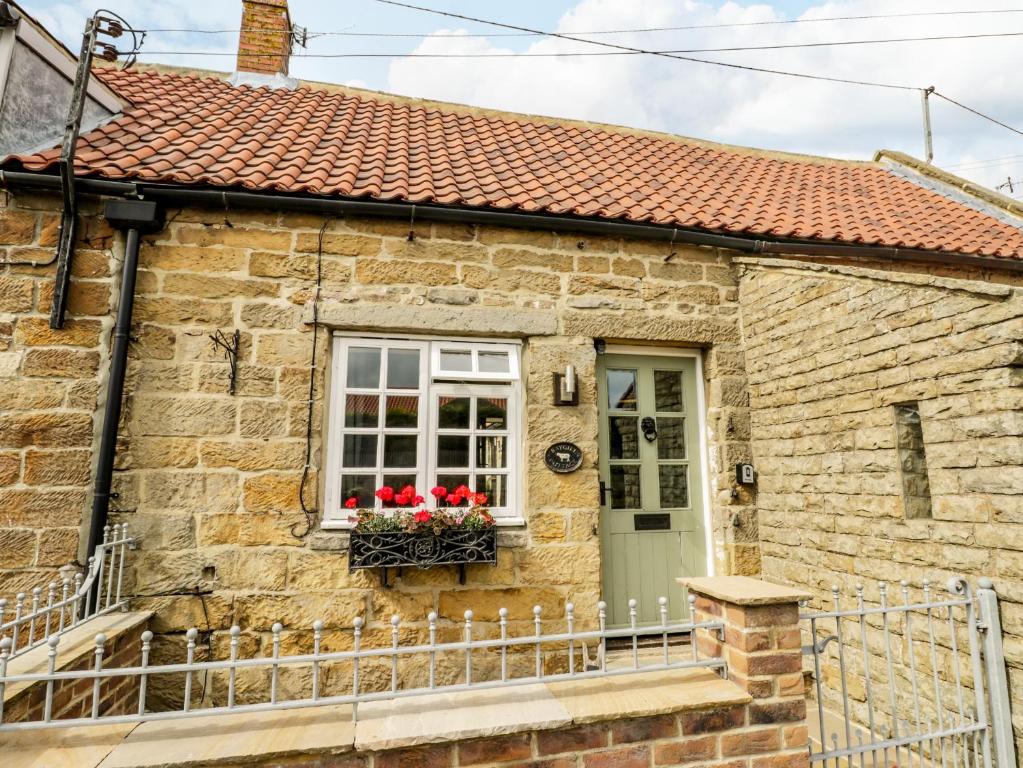 a stone house with a window and red flowers in a window box at Raygill Cottage in Whitby