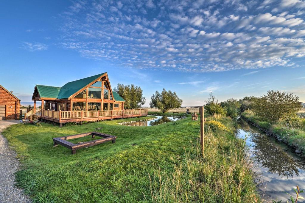 a wooden cabin with a green roof next to a river at Stunning Driggs Retreat with Private Hot Tub and Pond! in Driggs