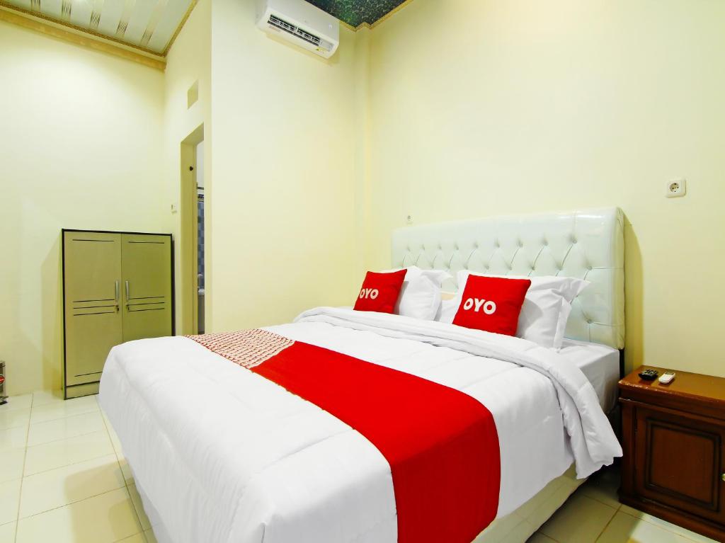 1 dormitorio con 1 cama blanca grande con almohadas rojas en OYO 90978 Khalifi Guesthouse Syariah en Padang