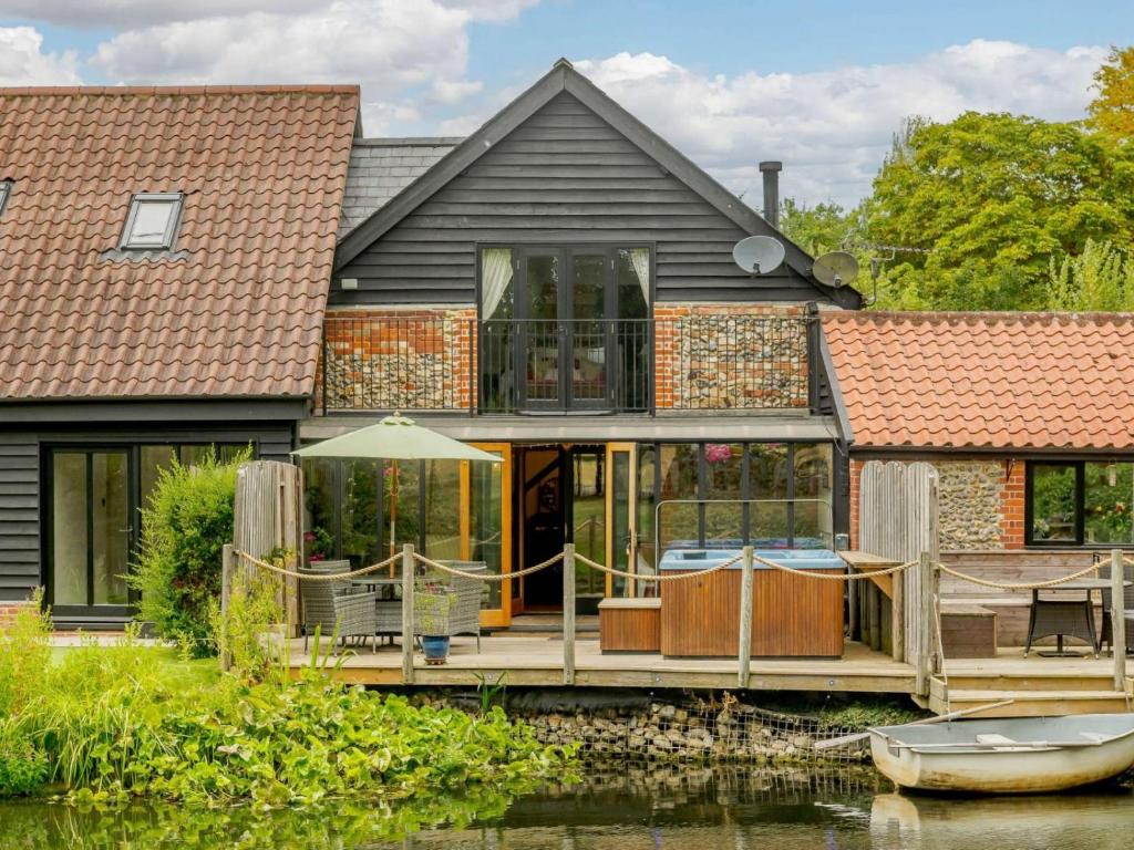 a house on the water with a deck and a boat at 16th Century Cartlodge with private hot tub in Diss