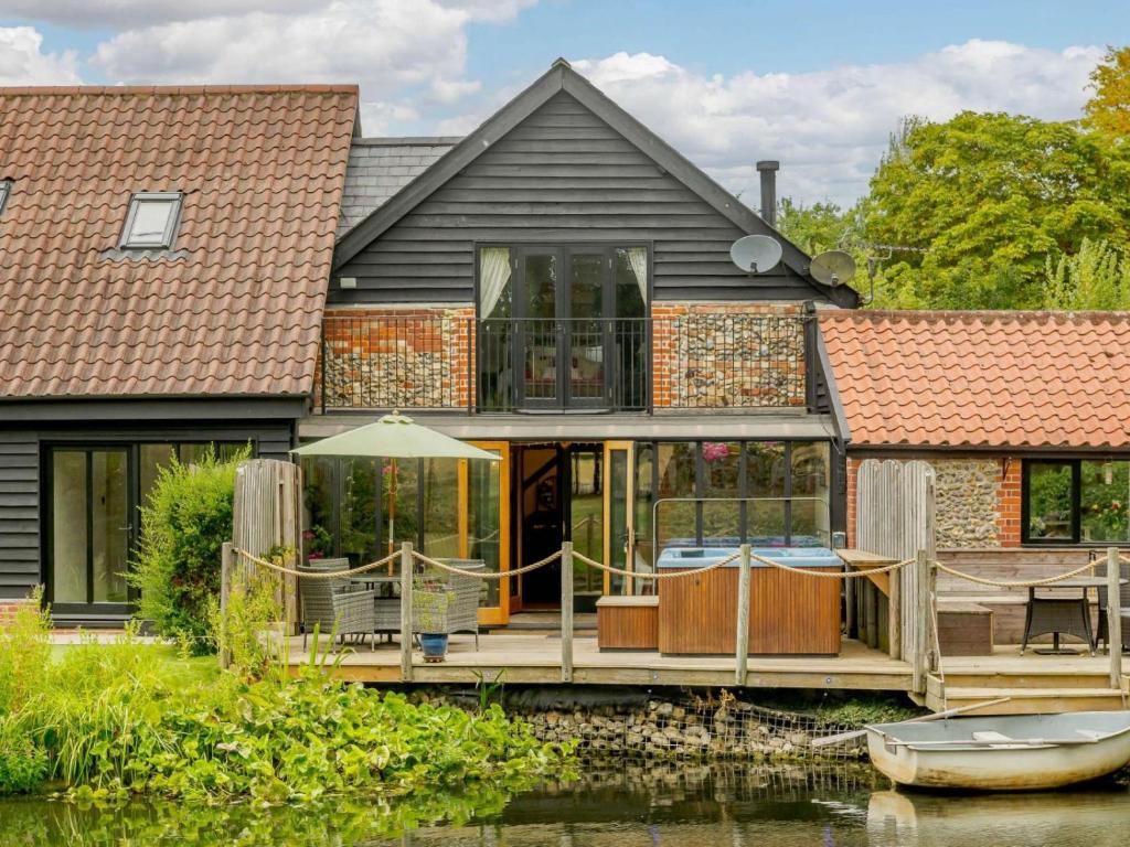 une maison sur l'eau avec une terrasse et un bateau dans l'établissement 16th Century Cartlodge with private hot tub, à Diss